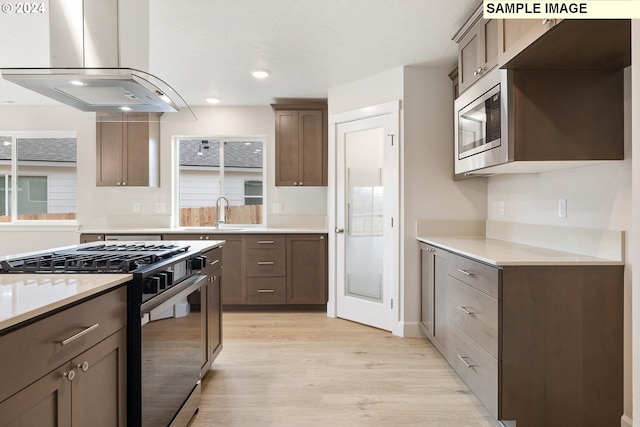 kitchen featuring sink, island range hood, light hardwood / wood-style flooring, stainless steel microwave, and gas range oven