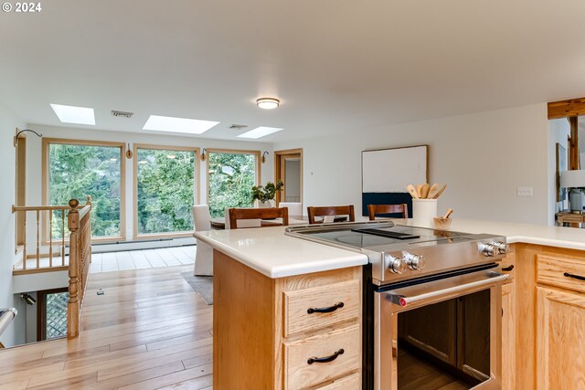 kitchen featuring light brown cabinets, light wood-type flooring, a skylight, and stainless steel range