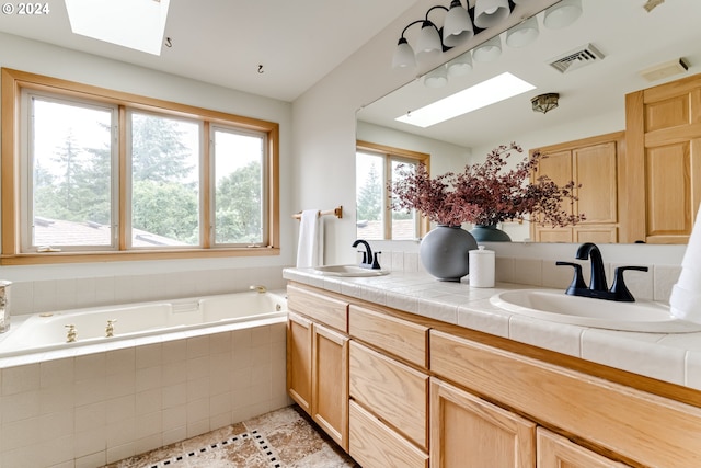 bathroom featuring tiled tub, vanity, a skylight, and a wealth of natural light