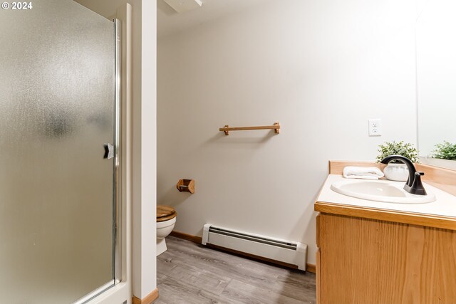 bathroom with vanity, wood-type flooring, a baseboard heating unit, walk in shower, and toilet