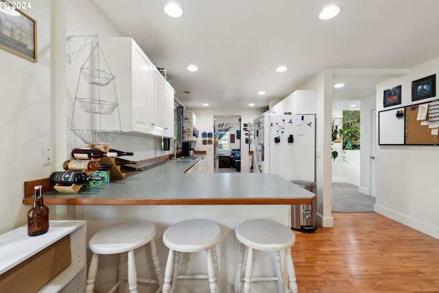 kitchen with recessed lighting, light wood-style floors, freestanding refrigerator, a sink, and a kitchen breakfast bar