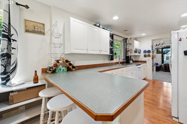 kitchen featuring white appliances, white cabinets, a breakfast bar area, light wood-style floors, and a sink