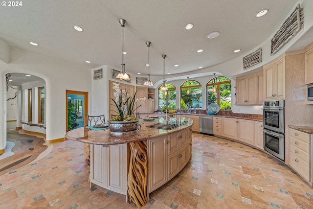 kitchen with pendant lighting, a center island, light stone counters, stainless steel appliances, and light brown cabinets