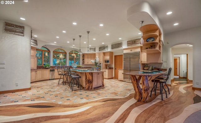 kitchen with hanging light fixtures, a kitchen breakfast bar, a center island, built in appliances, and light brown cabinetry