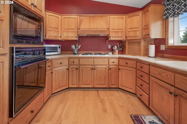 kitchen featuring sink, vaulted ceiling, light hardwood / wood-style flooring, and black appliances