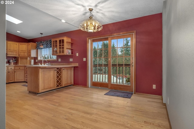 kitchen with decorative light fixtures, light hardwood / wood-style floors, kitchen peninsula, and vaulted ceiling