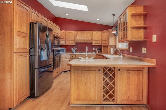 kitchen featuring custom exhaust hood, black appliances, vaulted ceiling with skylight, light hardwood / wood-style floors, and kitchen peninsula