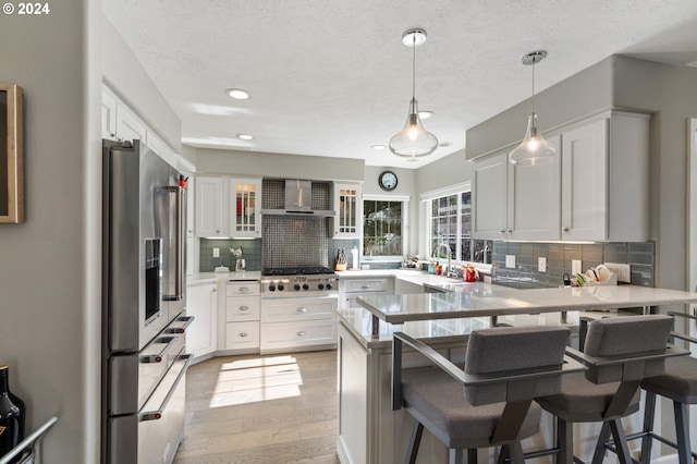 kitchen featuring decorative backsplash, appliances with stainless steel finishes, a peninsula, light wood-style floors, and white cabinets