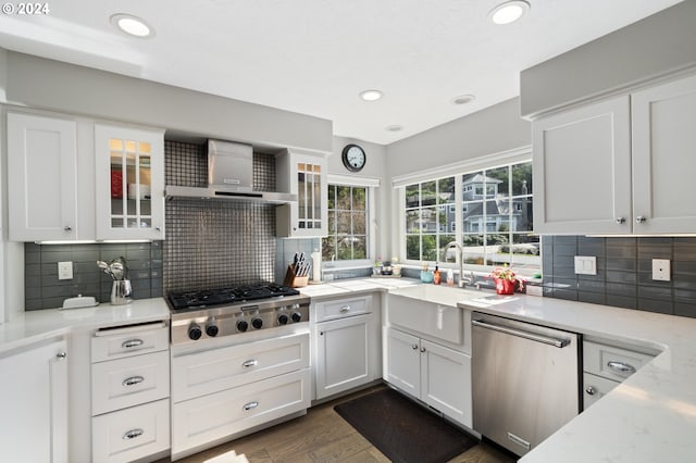 kitchen with stainless steel appliances, light stone countertops, wall chimney exhaust hood, and white cabinetry