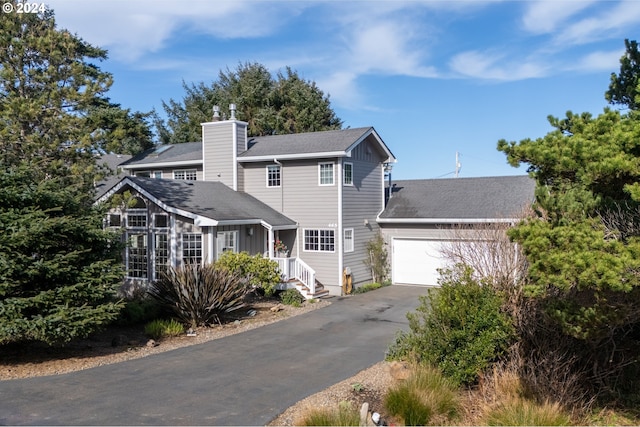 view of front of home featuring a shingled roof, aphalt driveway, an attached garage, and a chimney