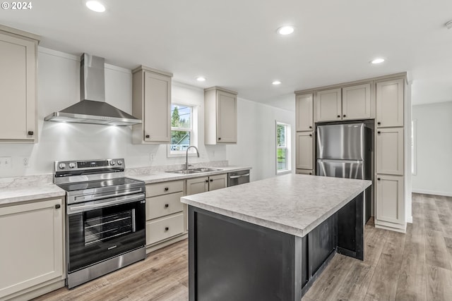 kitchen with wall chimney exhaust hood, light hardwood / wood-style floors, a kitchen island, appliances with stainless steel finishes, and sink