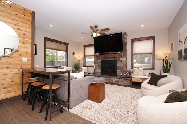 living room featuring ceiling fan, hardwood / wood-style floors, and a stone fireplace