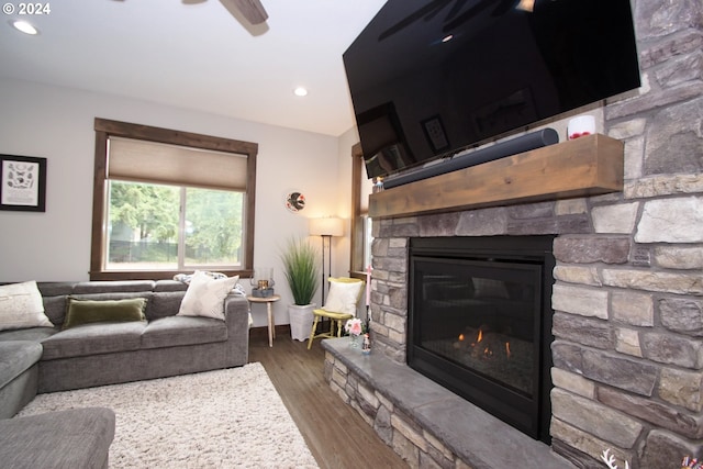 living room featuring ceiling fan, dark hardwood / wood-style flooring, and a stone fireplace