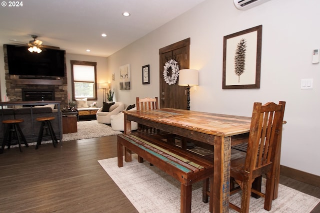 dining space with ceiling fan, dark wood-type flooring, and a stone fireplace