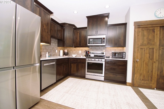 kitchen featuring appliances with stainless steel finishes, tasteful backsplash, sink, dark brown cabinets, and light hardwood / wood-style flooring