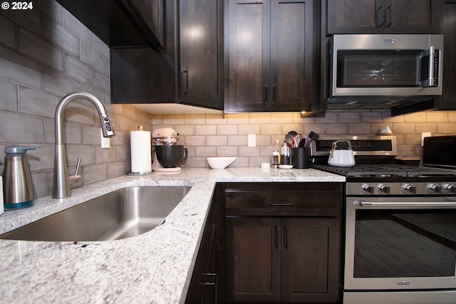 kitchen featuring sink, backsplash, light stone countertops, and appliances with stainless steel finishes