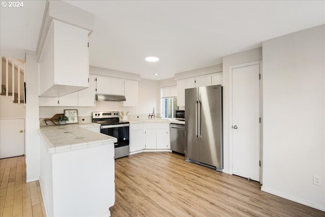 kitchen with tile counters, white cabinets, stainless steel appliances, and light wood-type flooring