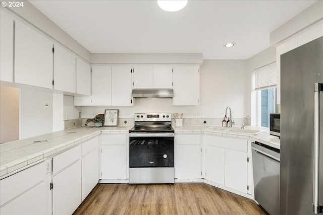 kitchen with stainless steel appliances, sink, light hardwood / wood-style floors, white cabinetry, and tile counters