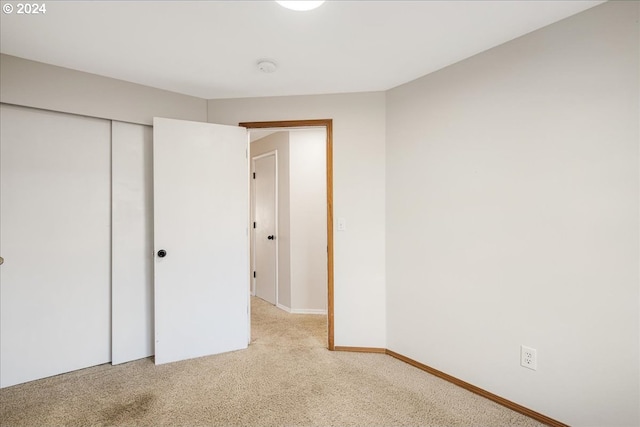 unfurnished bedroom with light colored carpet and a closet