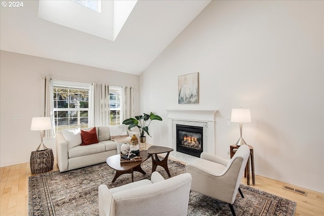 living room with a skylight, a high end fireplace, high vaulted ceiling, and wood-type flooring