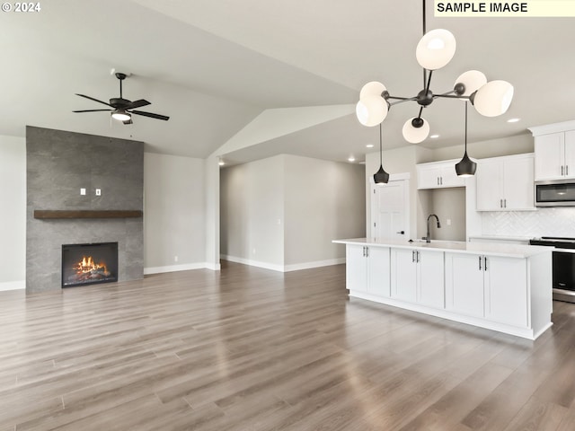 kitchen with lofted ceiling, a kitchen island with sink, light hardwood / wood-style floors, white cabinetry, and stainless steel appliances