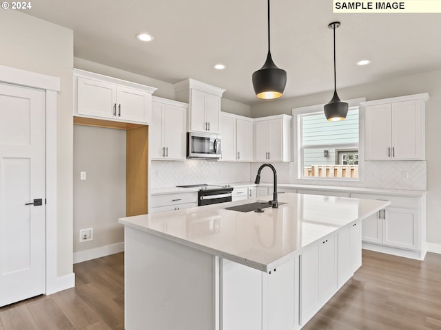 kitchen with appliances with stainless steel finishes, decorative light fixtures, white cabinets, light hardwood / wood-style floors, and an island with sink