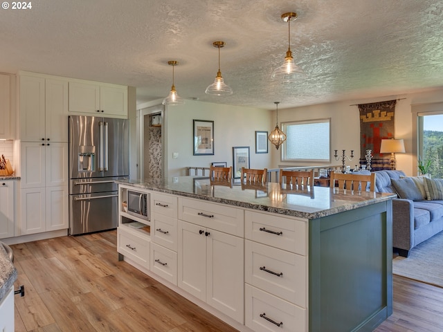 kitchen featuring white cabinetry, hanging light fixtures, stainless steel appliances, light stone counters, and light wood-type flooring