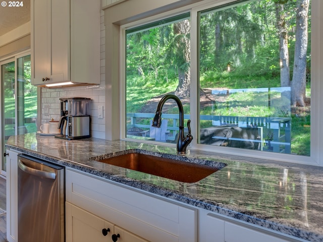 kitchen with decorative backsplash, stainless steel dishwasher, sink, dark stone countertops, and white cabinetry