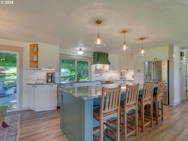 kitchen with white cabinets, a kitchen island, appliances with stainless steel finishes, and light hardwood / wood-style flooring