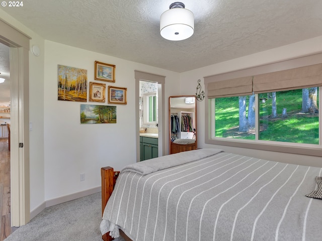 bedroom with ensuite bath, light colored carpet, and a textured ceiling