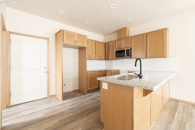 kitchen with light hardwood / wood-style floors, kitchen peninsula, tasteful backsplash, and sink