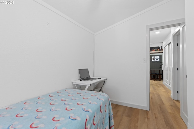 bedroom featuring baseboards, vaulted ceiling, light wood-style flooring, and crown molding