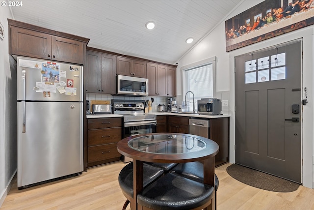 kitchen featuring stainless steel appliances, light wood-style floors, vaulted ceiling, a sink, and dark brown cabinetry