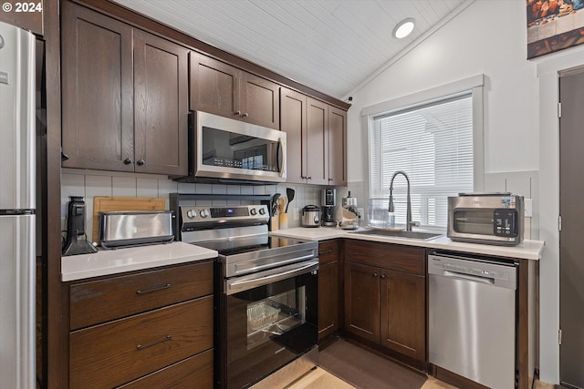 kitchen featuring lofted ceiling, a sink, light countertops, appliances with stainless steel finishes, and decorative backsplash