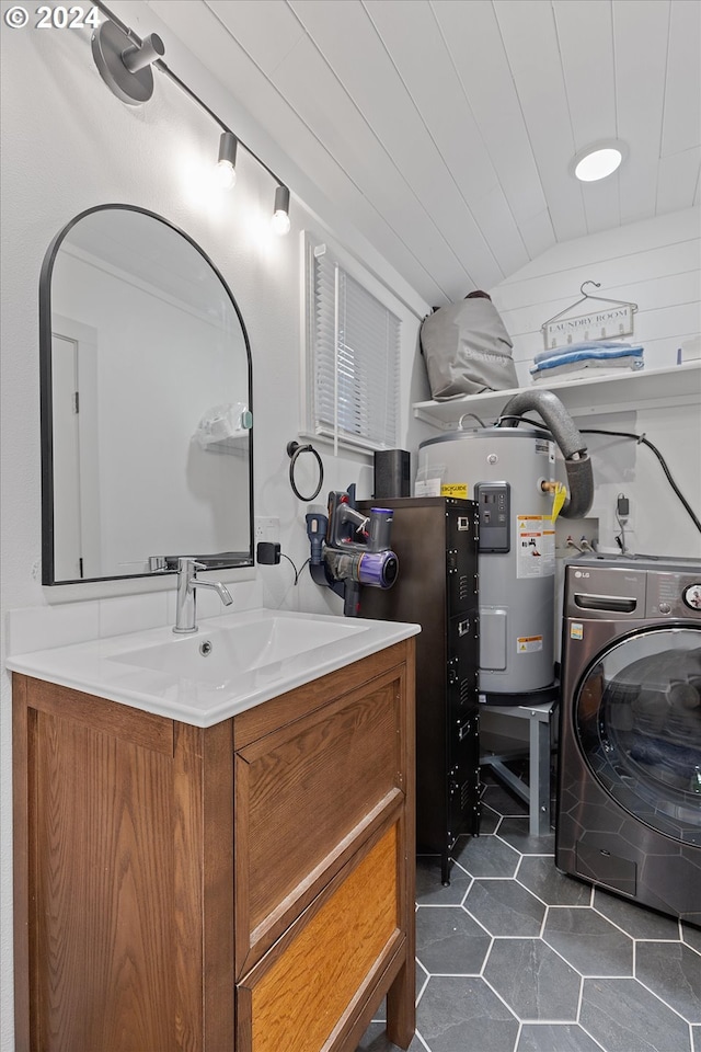 washroom featuring washer / dryer, dark tile patterned flooring, water heater, and a sink