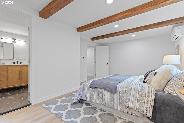 bedroom with sink, light wood-type flooring, a wall unit AC, connected bathroom, and beam ceiling