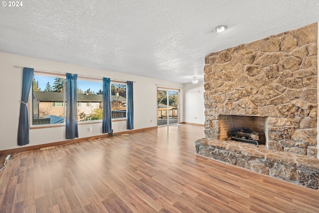 unfurnished living room featuring hardwood / wood-style floors, a textured ceiling, and a stone fireplace