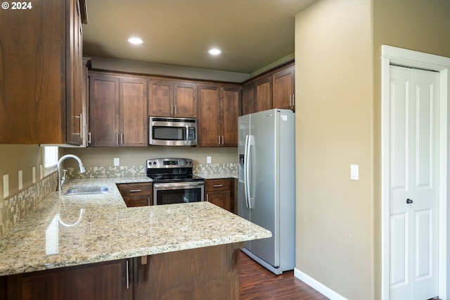 kitchen with dark hardwood / wood-style flooring, appliances with stainless steel finishes, kitchen peninsula, light stone counters, and sink