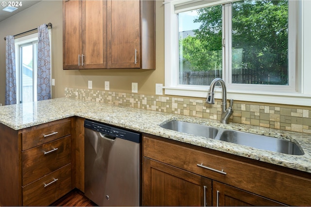 kitchen with kitchen peninsula, stainless steel dishwasher, light stone counters, backsplash, and sink