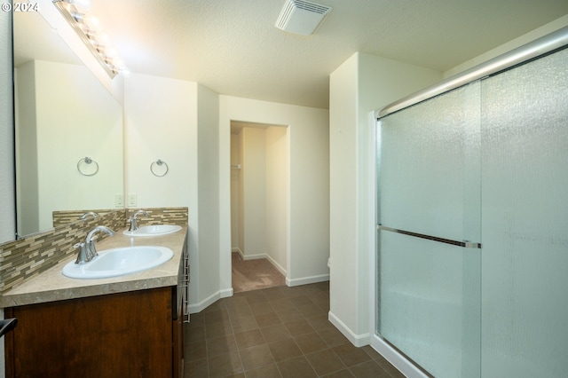 bathroom featuring tile floors, dual bowl vanity, an enclosed shower, and backsplash