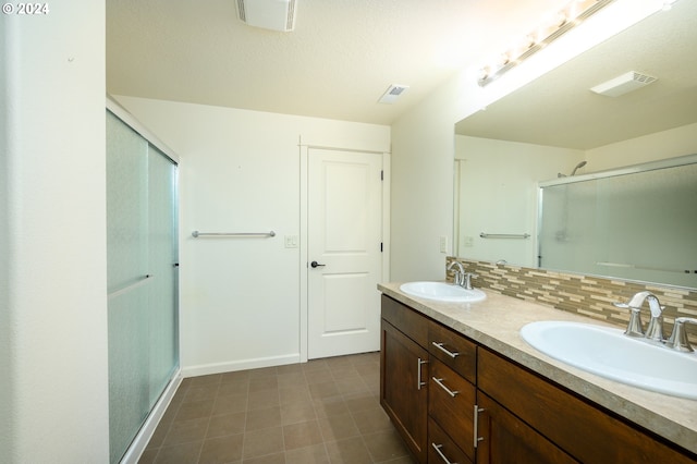 bathroom with vanity with extensive cabinet space, tasteful backsplash, a shower with shower door, tile flooring, and double sink