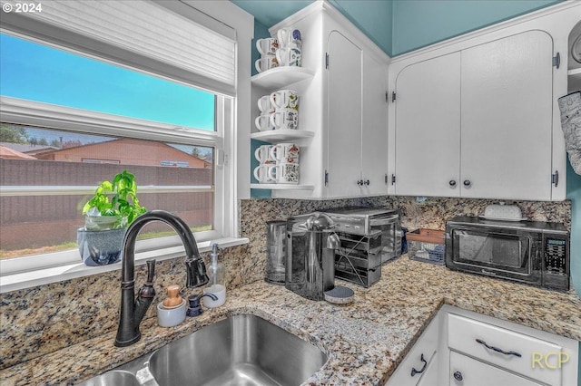 kitchen featuring light stone countertops, sink, white cabinets, and decorative backsplash