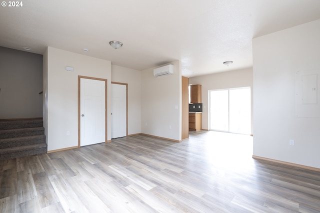 unfurnished bedroom with an AC wall unit, electric panel, and light wood-type flooring