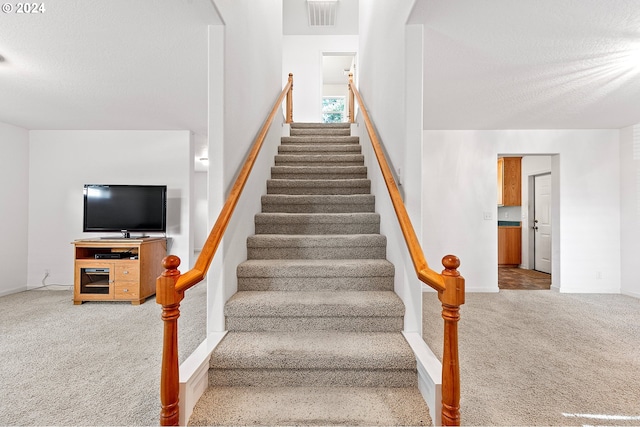 stairway with carpet floors and a textured ceiling