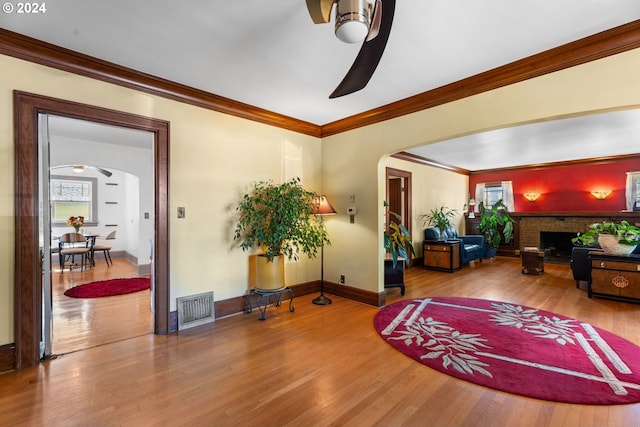 living room featuring hardwood / wood-style floors, a brick fireplace, ceiling fan, and crown molding