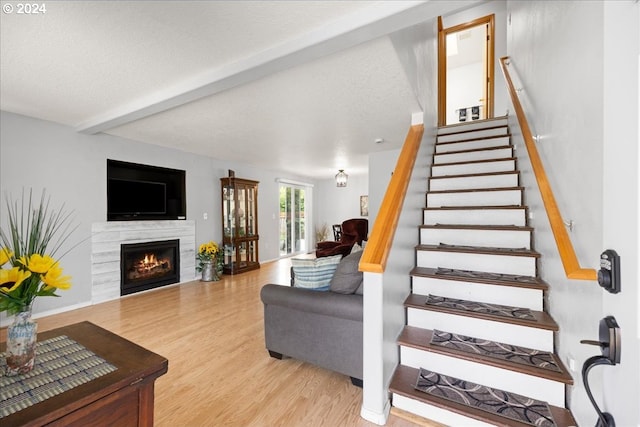 staircase featuring beamed ceiling, hardwood / wood-style flooring, a textured ceiling, and a premium fireplace