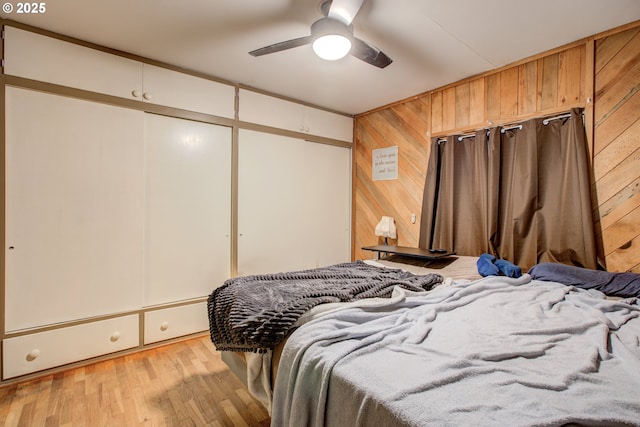 bedroom featuring light hardwood / wood-style floors, ceiling fan, and wooden walls