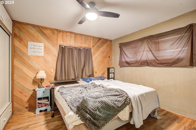 bedroom with light hardwood / wood-style flooring, ceiling fan, and wooden walls