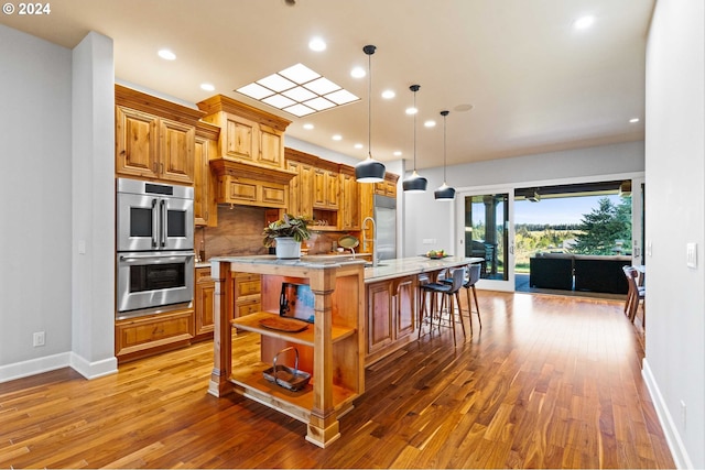 kitchen with a kitchen breakfast bar, hardwood / wood-style floors, stainless steel appliances, a center island with sink, and backsplash