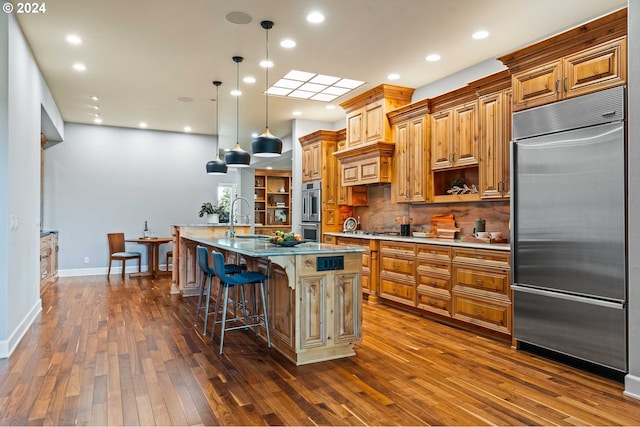 kitchen featuring appliances with stainless steel finishes, dark wood-type flooring, a center island with sink, and backsplash